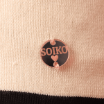 Pessoa usando Vestido Aiko creme ombro a ombro com detalhes em laço preto, meia-calça branca com padrão delicado, polainas brancas e sapatos Mary Jane creme, em frente a fundo rosa.